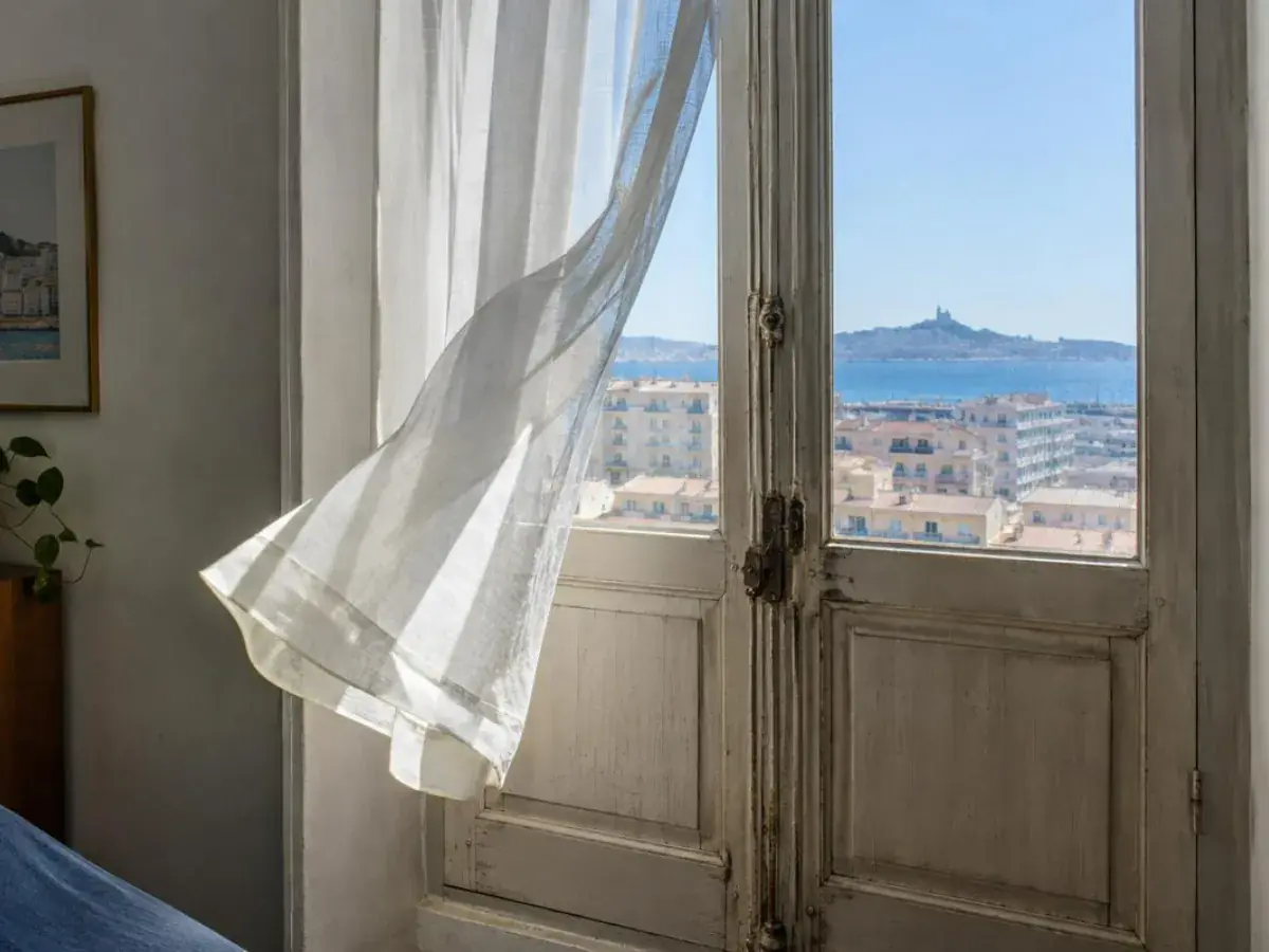 Fenêtre bois d’appartement marseillais fermée, rideau soulevé par un courant d’air un jour de vent