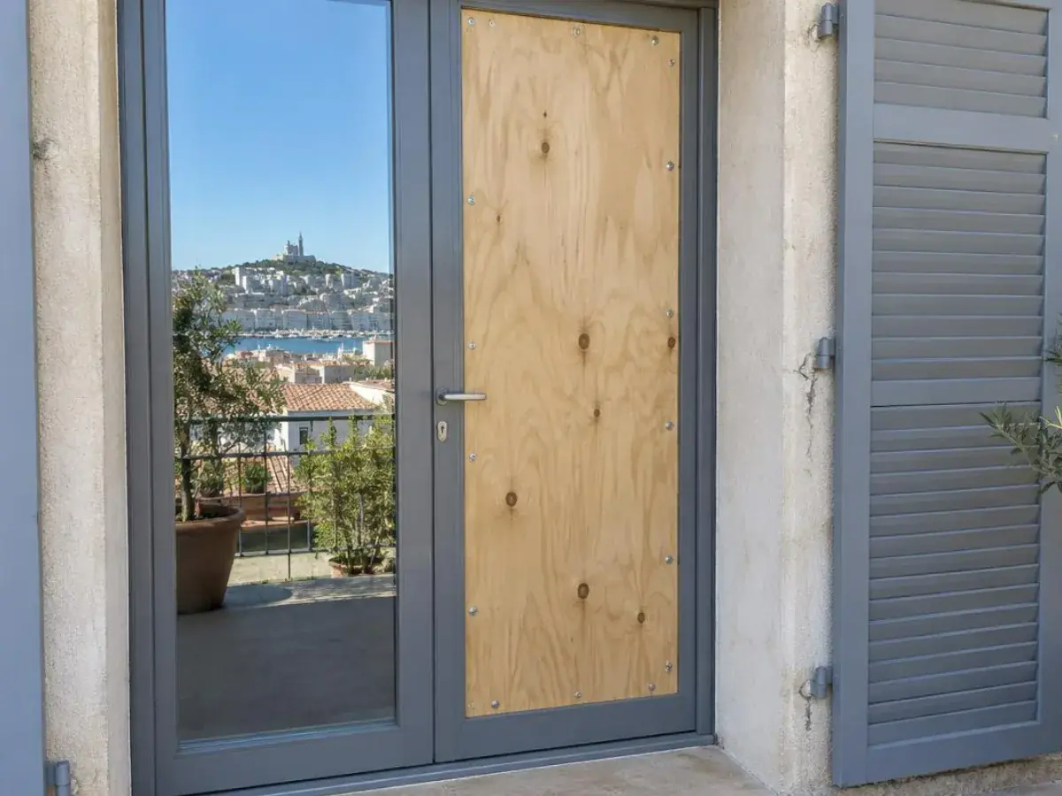Panneau provisoire vissé à la place d'une vitre brisée sur une porte-fenêtre en aluminium, intervention à Marignane